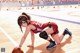 A woman in a red and black uniform crouching on a basketball court.