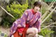 A woman in a purple and red kimono sitting on a rock.