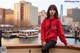 A woman in a red hoodie sitting on a railing by the water.